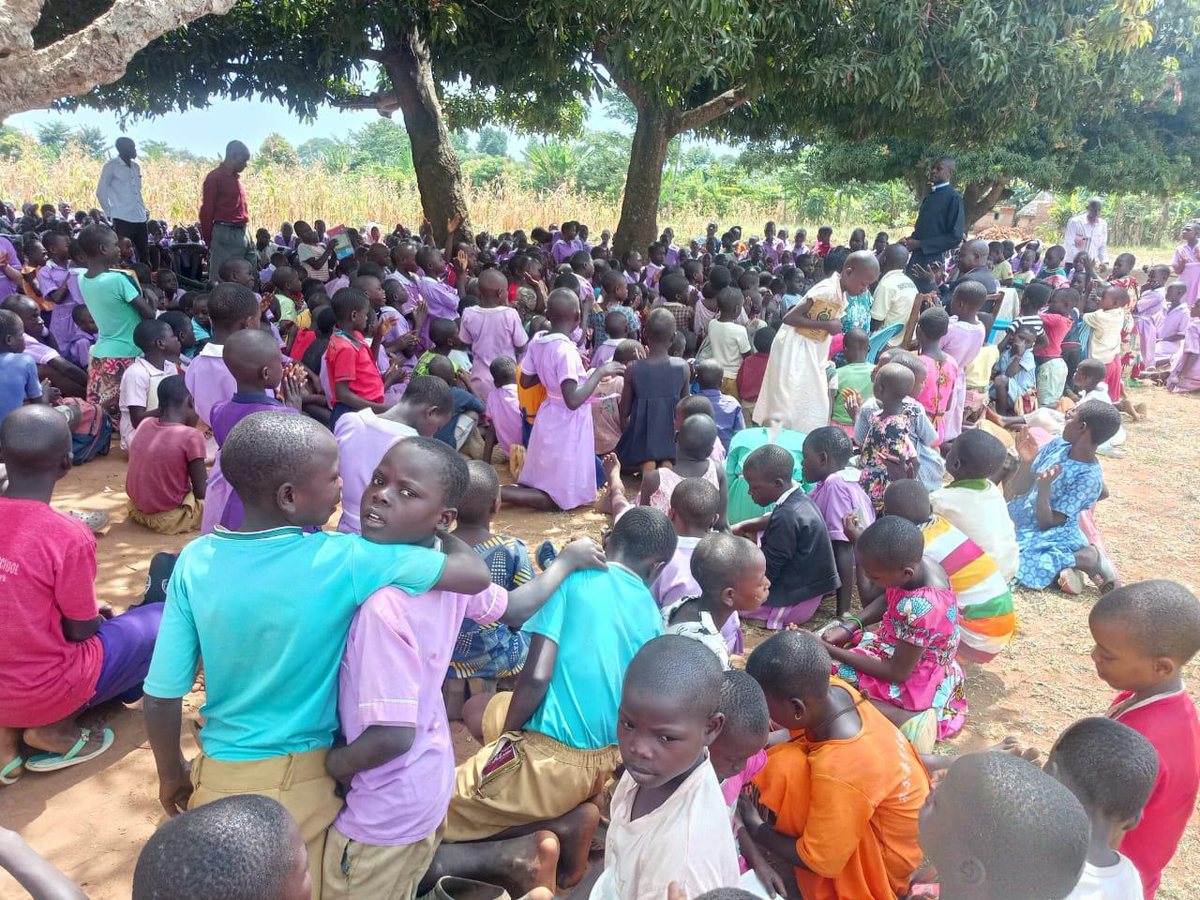 Children seated together under trees during an outreach